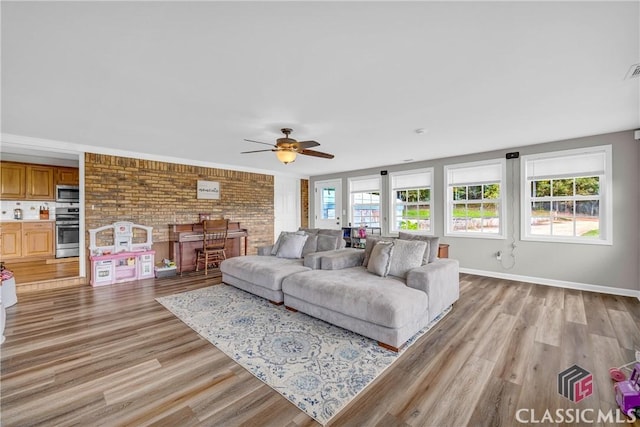 living area with a ceiling fan, light wood-type flooring, baseboards, and brick wall