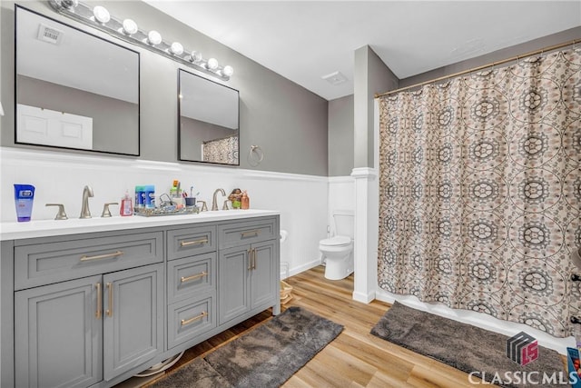 bathroom with double vanity, visible vents, wainscoting, toilet, and wood finished floors