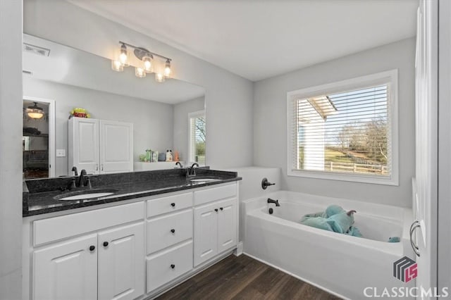 bathroom with double vanity, visible vents, wood finished floors, a garden tub, and a sink