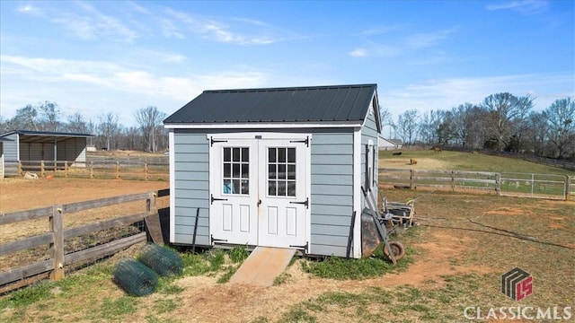 view of outbuilding with a rural view, an outdoor structure, and fence