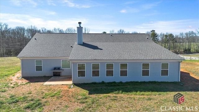 rear view of house featuring a yard, roof with shingles, a chimney, and a patio