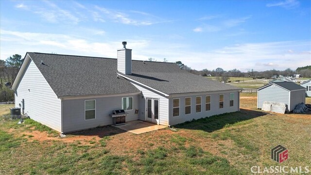 rear view of property featuring a patio, a shingled roof, a chimney, and a lawn