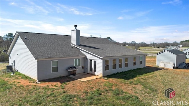 rear view of property featuring roof with shingles, a chimney, central AC unit, and a yard