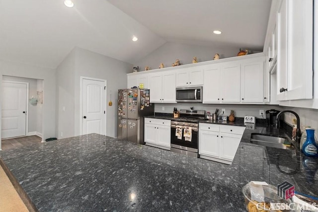 kitchen featuring white cabinets, appliances with stainless steel finishes, dark stone countertops, vaulted ceiling, and a sink