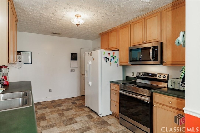 kitchen featuring stainless steel appliances, dark countertops, visible vents, a sink, and baseboards