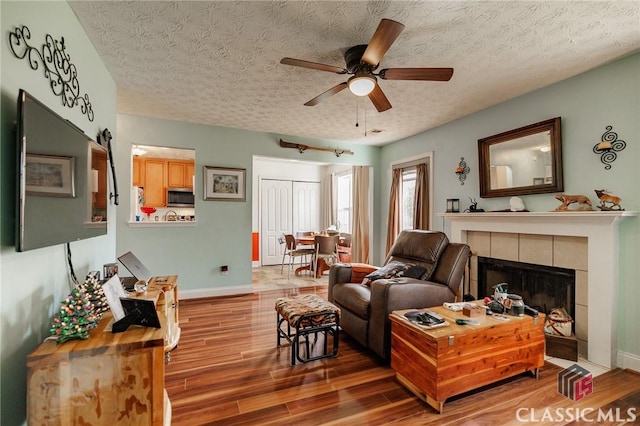 living room with a textured ceiling, a fireplace, wood finished floors, and baseboards