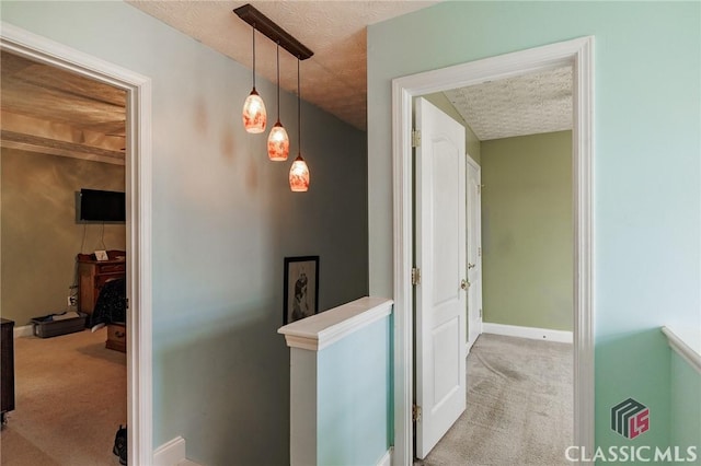 corridor featuring a textured ceiling, baseboards, carpet flooring, and an upstairs landing