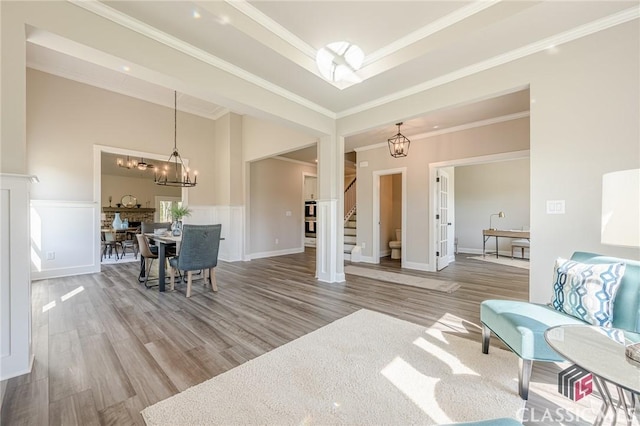living area featuring a notable chandelier, ornamental molding, wood finished floors, stairs, and a wainscoted wall