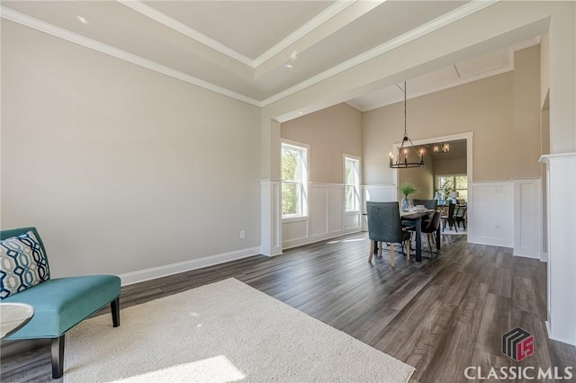 living area with a notable chandelier, ornamental molding, dark wood-style floors, a wainscoted wall, and a decorative wall