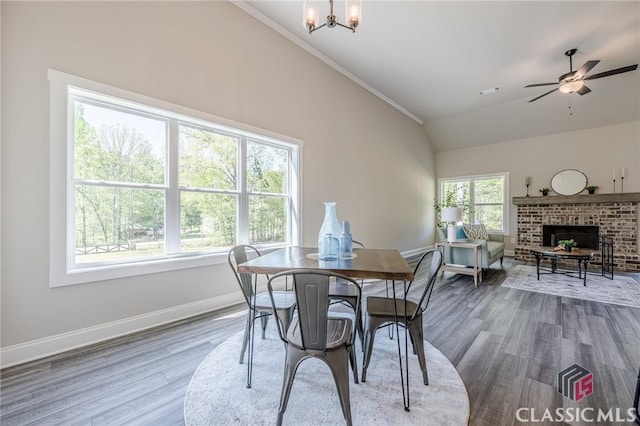 dining area with baseboards, a brick fireplace, wood finished floors, and ceiling fan with notable chandelier