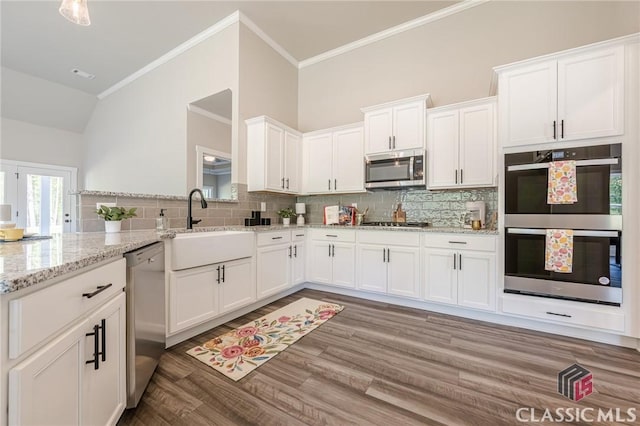 kitchen with stainless steel appliances, white cabinetry, backsplash, and wood finished floors