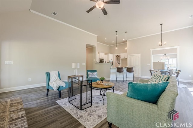 living room with ceiling fan with notable chandelier, ornamental molding, baseboards, and dark wood-style floors
