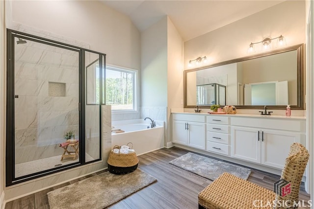 full bathroom featuring a shower stall, a bath, wood finished floors, and double vanity
