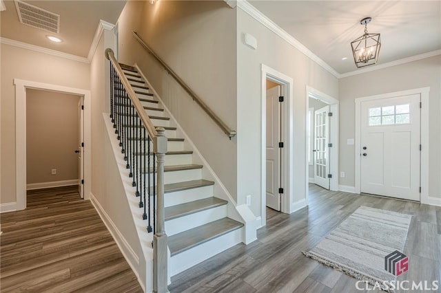 entrance foyer with visible vents, a notable chandelier, ornamental molding, stairway, and wood finished floors