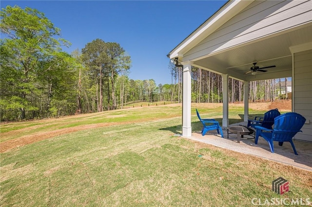 view of yard featuring an outdoor fire pit, a view of trees, ceiling fan, and a patio area