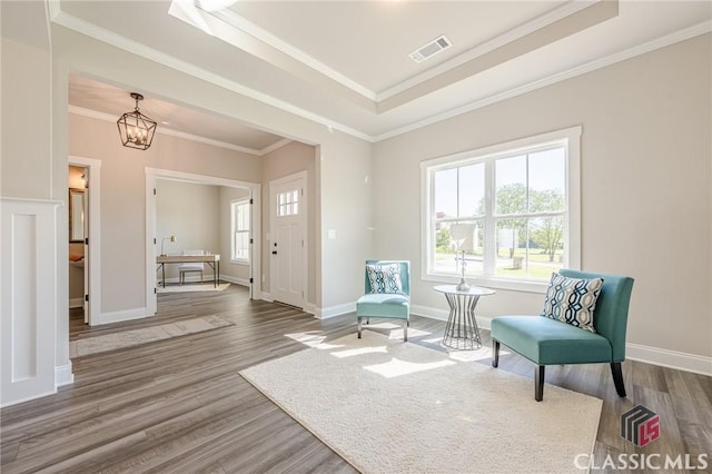 sitting room with a tray ceiling, wood finished floors, a notable chandelier, and ornamental molding