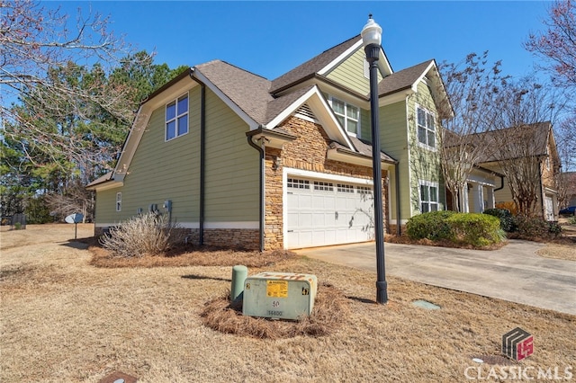 view of side of property featuring a garage, stone siding, a shingled roof, and concrete driveway