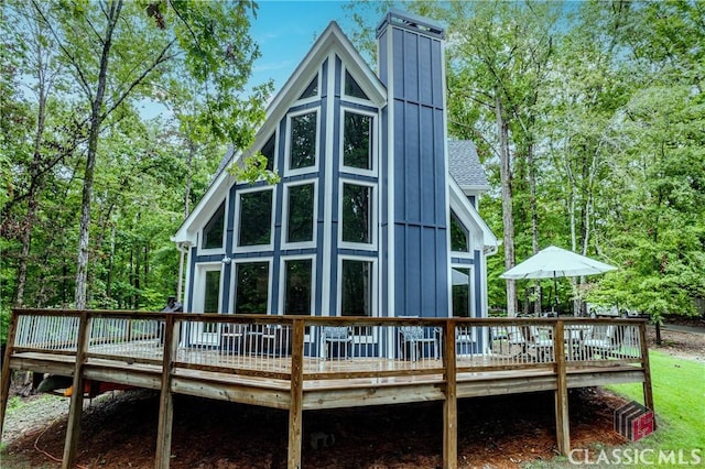 rear view of property featuring board and batten siding, a deck with water view, a chimney, and roof with shingles