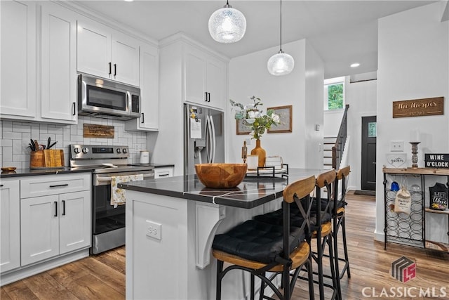 kitchen with stainless steel appliances, dark countertops, a breakfast bar, and wood finished floors