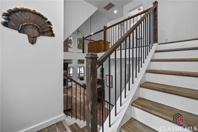 staircase with recessed lighting, visible vents, a high ceiling, wood finished floors, and baseboards