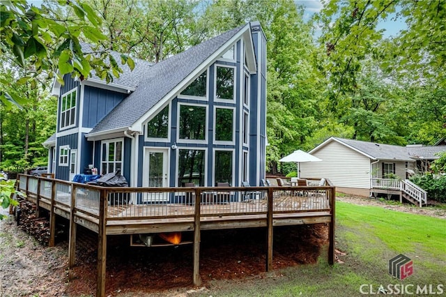 back of house featuring a shingled roof, a lawn, a deck, and board and batten siding