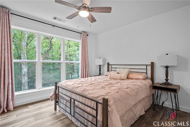 bedroom featuring baseboards, multiple windows, visible vents, and wood finished floors