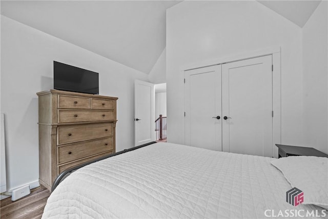 bedroom with high vaulted ceiling, a closet, wood finished floors, and baseboards