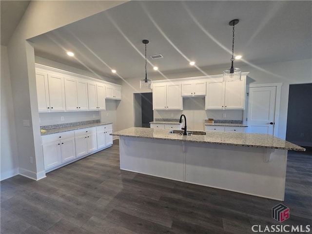 kitchen featuring white cabinets, light stone countertops, dark wood-style flooring, and a sink