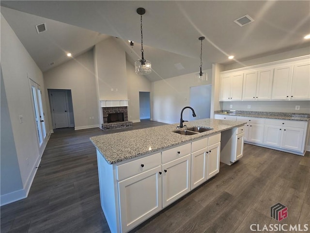 kitchen with a fireplace, visible vents, dark wood-type flooring, a kitchen island with sink, and a sink