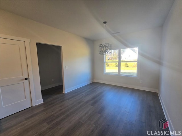 unfurnished dining area featuring dark wood-type flooring, an inviting chandelier, and baseboards