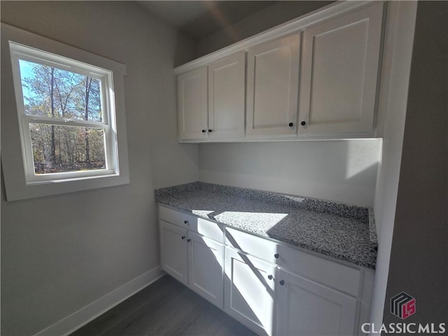 kitchen with light stone countertops, white cabinetry, baseboards, and dark wood-style flooring