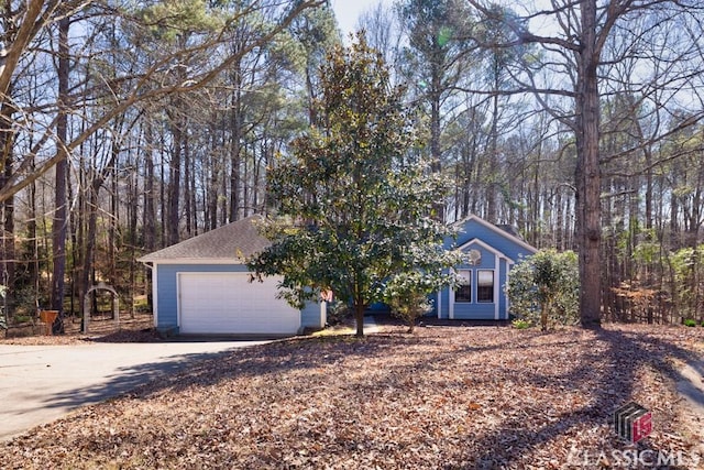 view of property hidden behind natural elements with a garage and concrete driveway