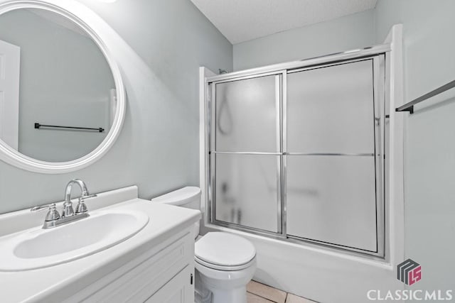 full bathroom featuring bath / shower combo with glass door, toilet, vanity, a textured ceiling, and tile patterned flooring