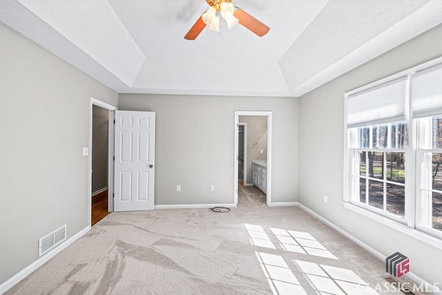 unfurnished bedroom featuring light carpet, a tray ceiling, visible vents, and baseboards