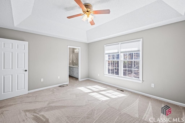 unfurnished bedroom with carpet floors, a tray ceiling, visible vents, ensuite bath, and baseboards