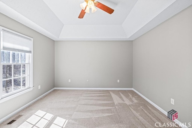 spare room with ceiling fan, light colored carpet, visible vents, baseboards, and a raised ceiling