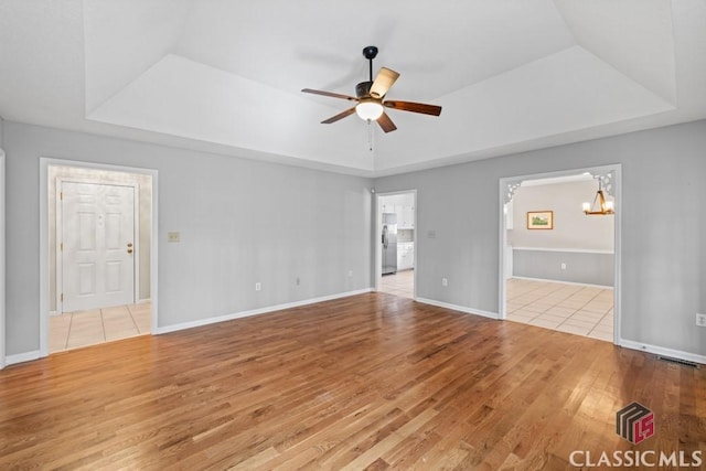 interior space with ceiling fan with notable chandelier, a tray ceiling, baseboards, and wood finished floors