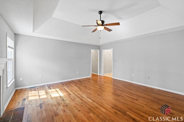 empty room with a tray ceiling, a fireplace, baseboards, and wood finished floors