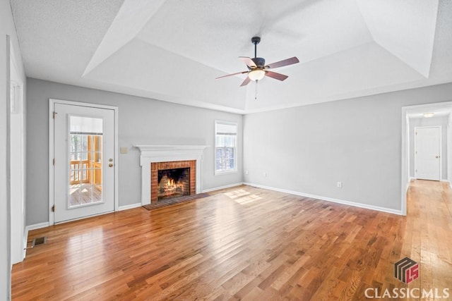 unfurnished living room with a tray ceiling, a brick fireplace, light wood-style flooring, and visible vents