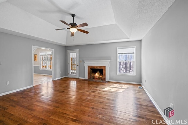 unfurnished living room with wood-type flooring, plenty of natural light, a raised ceiling, and a brick fireplace