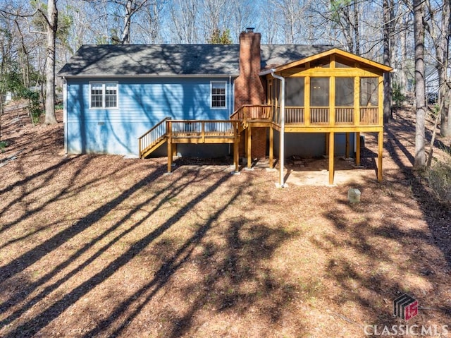 rear view of house featuring a deck, a chimney, stairs, and a sunroom