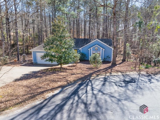 ranch-style home with concrete driveway, a forest view, and an attached garage