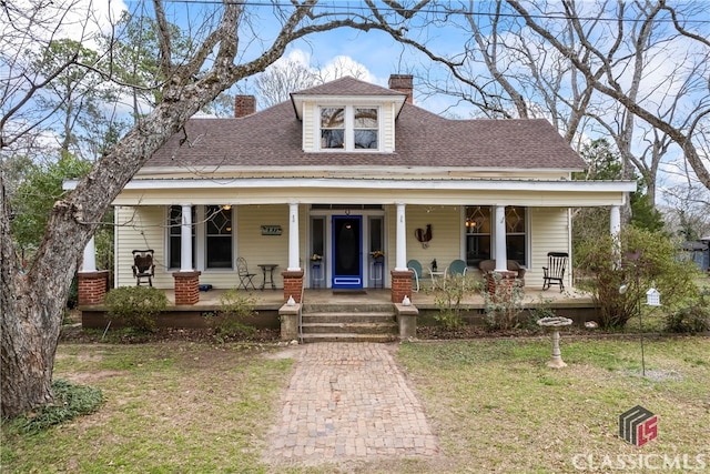 view of front of property featuring covered porch, roof with shingles, a chimney, and a front yard