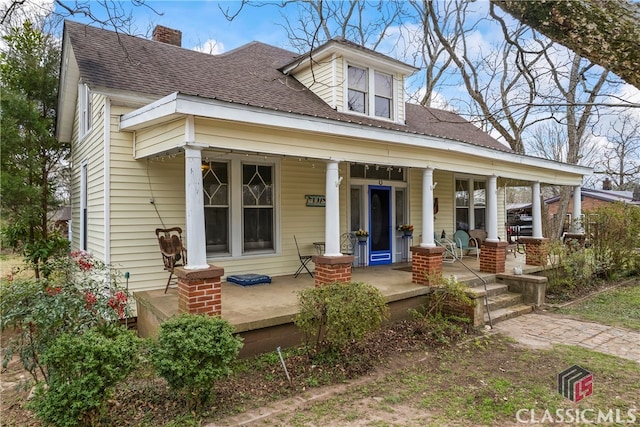 view of front of house featuring covered porch, a shingled roof, and a chimney