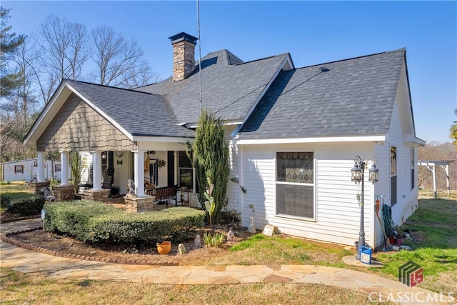 back of property with covered porch, a shingled roof, and a chimney