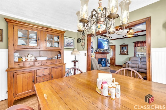 dining space featuring wainscoting, ornamental molding, a fireplace, and light wood-style flooring