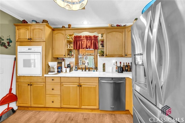 kitchen featuring a wainscoted wall, stainless steel appliances, light wood-style floors, open shelves, and a sink