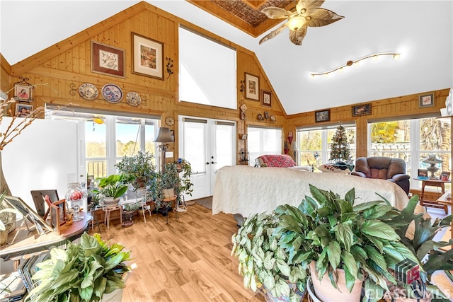 bedroom with high vaulted ceiling, light wood finished floors, and wooden walls