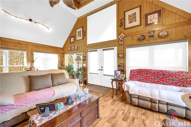 bedroom featuring wood walls, light wood-style flooring, and high vaulted ceiling