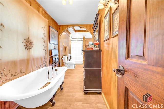 bathroom with a soaking tub, wooden walls, and wood finished floors